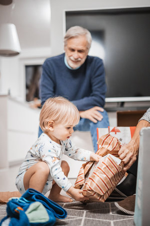 Cute little blond Caucasian toddler unpacking Christmas or Birthday present. Adorable small infant baby boy opening gift.の写真素材