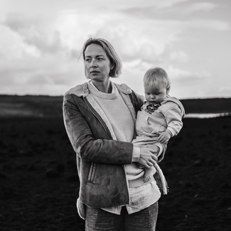 Mother enjoying winter vacations playing with his infant baby boy son on black sandy volcanic beach of Janubio on Lanzarote island, Spain on windy overcast day. Family travel vacations conceptの写真素材
