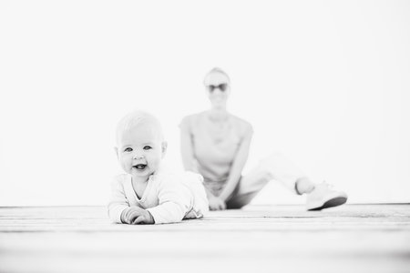 Happy family. Young mother playing with her baby boy infant oudoors on sunny autumn day. Portrait of mom and little son on wooden platform by lake. Positive human emotions, feelings, joyの写真素材