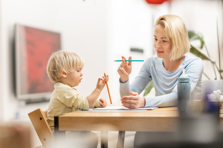 Caring young Caucasian mother and small son drawing painting in notebook at home together. Loving mom or nanny having fun learning and playing with her little 1,5 year old infant baby boy childの写真素材