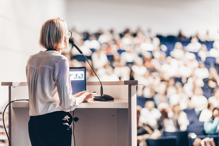 Female speaker giving a talk on corporate business conference. Unrecognizable people in audience at conference hall. Business and Entrepreneurship eventの写真素材