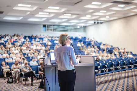 Female speaker giving a talk on corporate business conference. Unrecognizable people in audience at conference hall. Business and Entrepreneurship eventの写真素材
