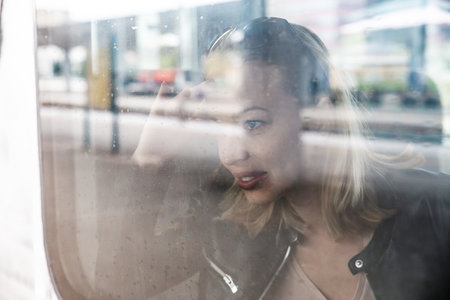 Woman traveler contemplating outdoor view from window of train. Young lady on commute travel to work sitting in bus or trainの写真素材
