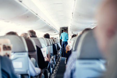 Interior of airplane with passengers on seats and stewardess in uniform walking the aisle, serving people. Commercial economy flight service conceptの写真素材