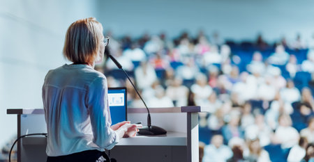 Female speaker giving a talk on corporate business conference. Unrecognizable people in audience at...