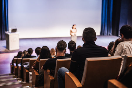 Business and entrepreneurship symposium. Female speaker giving a talk at business meeting. Audience in conference hall. Rear view of unrecognized participant in audience.の写真素材
