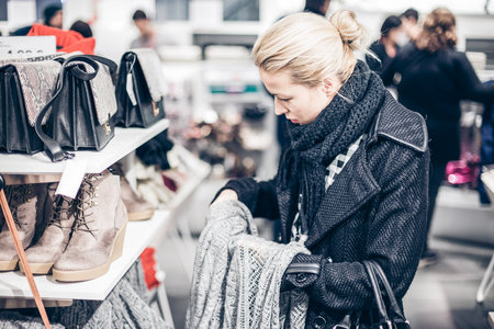 Woman shopping clothes. Shopper looking at clothing indoors in store. Beautiful blonde caucasian female model.の写真素材