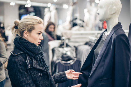 Woman shopping clothes. Shopper looking at clothing indoors in store. Beautiful blonde caucasian female model.の写真素材
