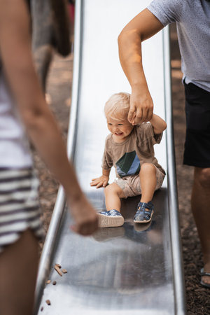 Parent hand holding little infant baby boy child while sliding on urban playground on a sunny summer day. Family joy and happiness concept.の写真素材