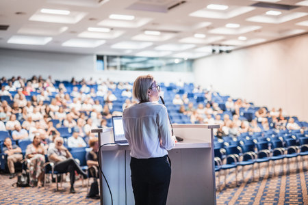Female speaker giving a talk on corporate business conference. Unrecognizable people in audience at conference hall. Business and Entrepreneurship eventの写真素材