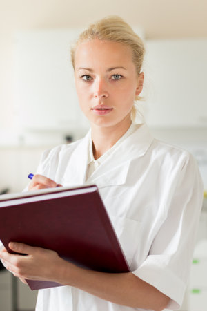 Portrait of young, confident female health care professional taking notes during inventory in scientific laboratory or medical doctors office.の写真素材