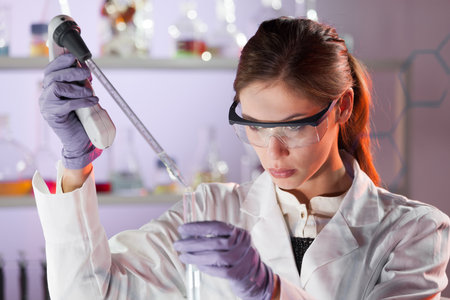 Life scientists researching in laboratory. Focused female life science professional pipetting solution into the glass cuvette. Lens focus on researchers eyes. Healthcare and biotechnology concept.の写真素材