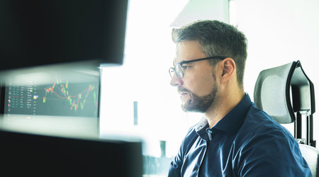 Male stock broker trading online watching charts and data analyses on multiple computer screens.の写真素材