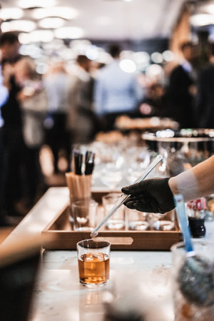 Expert barman is making cocktail at business banquet event in hotel conference center. Blurred businesspeople at banquet event business meeting event in the background.の写真素材