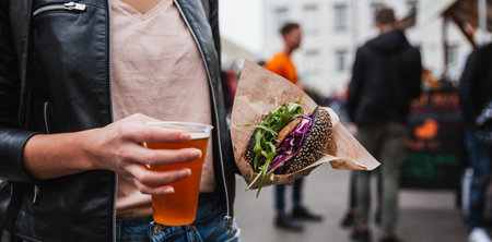 Close up of woman hands holding delicious organic salmon vegetarian burger and homebrewed IPA beer on open air beer and burger urban street food festival in Ljubljana, Sloveniaの写真素材