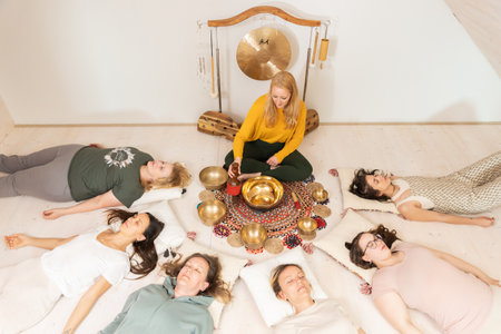 Group therapy session with Tibetan singing bowls for group of women lying on wooden floor surrounded by copper bowls. Meditation and relaxationの写真素材