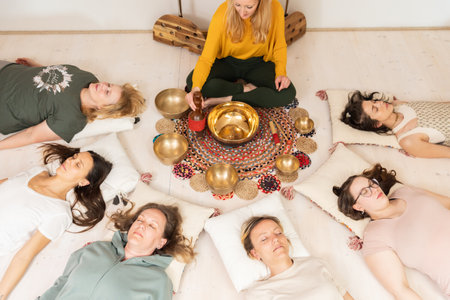 Group therapy session with Tibetan singing bowls for group of women lying on wooden floor surrounded by copper bowls. Meditation and relaxationの写真素材