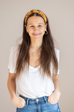 Portrait of confident beautiful woman with long brown hair, wearing casual clothes, standing in relaxed pose with hands in pockets, smiling with white teeth at camera, studio backgroundの写真素材