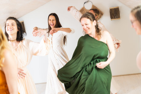 Group of cheerful women all ages, happy people dancing together wearing traditional colorful dresses and hippy clothes. Free people enjoying leisure activity, emphasizing friendship, fun, movement.の写真素材