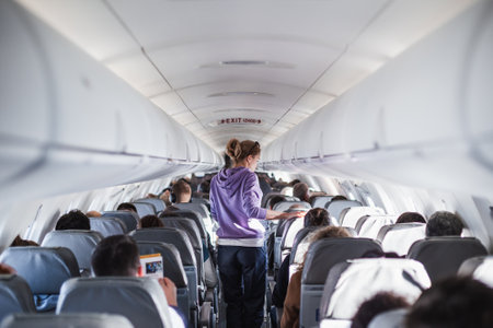 Interior of airplane with passengers on seats and female traveler walking the aisle. Commercial...