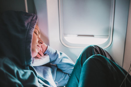 Tired blonde casual caucasian woman wearing sporty hoodie napping on seat while traveling by airplane. Commercial transportation by planes. Authentic image of real peopleの写真素材