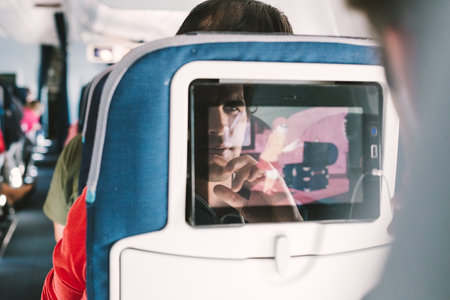 Reflection of a passenger on an airplane touch screen monitor while watching cartoon during long flight. Entertainment service system in aircraftの写真素材