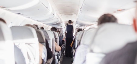 Interior of airplane with passengers on seats and stewardess in uniform walking the aisle, serving people. Commercial economy flight service conceptの写真素材