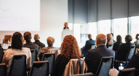 Female speaker giving a talk on corporate business conference. Unrecognizable people in audience at conference hall. Business and Entrepreneurship eventの写真素材