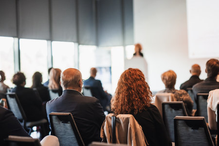 Business and entrepreneurship symposium. Female speaker giving a talk at business meeting. Audience in conference hall. Rear view of unrecognized participant in audience.の写真素材