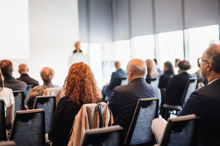 Business and entrepreneurship symposium. Female speaker giving a talk at business meeting. Audience in conference hall. Rear view of unrecognized participant in audience.の写真素材