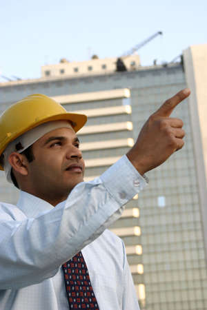 Young Indian Engineer with Vision looking up and pointing at a high rise building