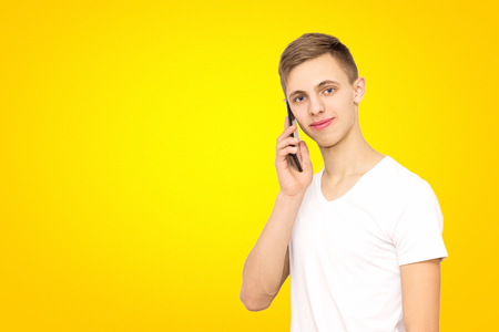 portrait of a guy talking on the phone in the studio on a yellow background, isolate, a man on a yellow background with a phone with a place under the inscriptionの写真素材