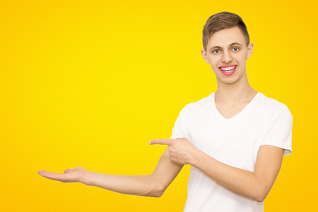 guy in white t-shirt shows advertising with his hands left in the studio on a yellow beautiful background advertising a young guyの写真素材