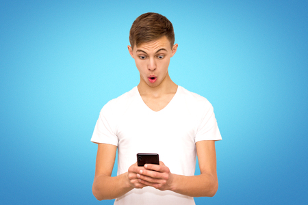 surprised guy in white t-shirt with telephone, isolate, man on blue background in studio with telephoneの写真素材