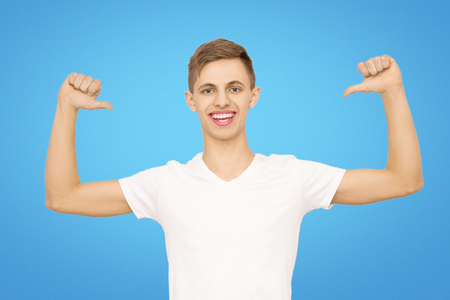 a guy in a white T-shirt with his hands up in the studio on a blue background, isolate, parer shows his fingerの写真素材