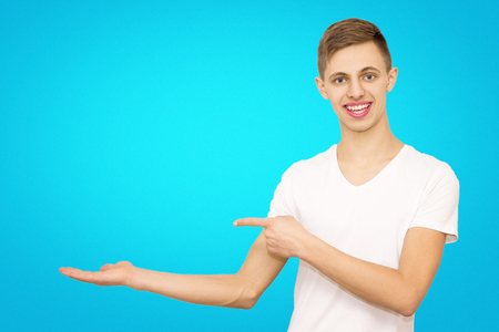 guy in white t-shirt shows advertising with his hands left in a studio on a blue beautiful background advertising a young guyの写真素材