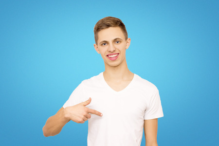 guy in a white T-shirt shows his finger at himself in the studio on a blue backgroundの写真素材