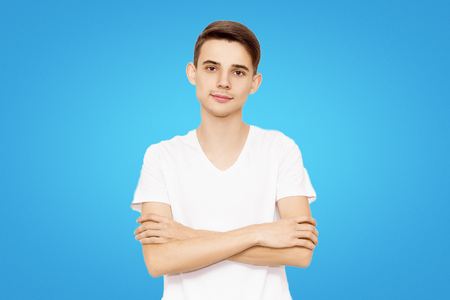 guy in a white T-shirt folded hands isolated on a blue background, friendly manの写真素材