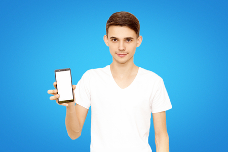 the guy in the white T-shirt advertises the phone, on a blue background in the studio. man with phoneの写真素材