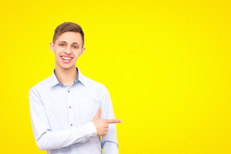 a guy in a blue shirt advertises a product, isolated on a yellow background, a man points his finger at an empty place under the inscriptionの写真素材