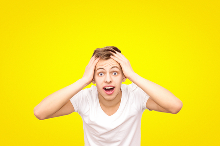 guy in white in a white T-shirt holding his head, isolated on a yellow background, pensive guyの写真素材