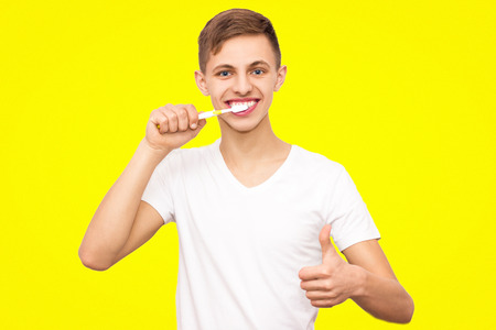 a guy in a white T-shirt brushing his teeth, isolated on a yellow background, a man caring for his healthの写真素材