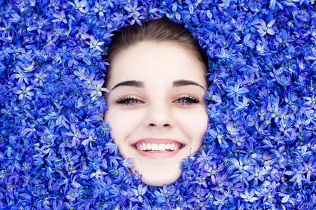 the girl is covered with blue spring flowers, the girl looks out from under the flowers. beautiful...
