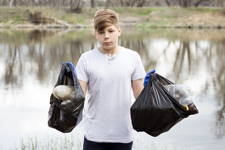 young volunteer guy picks up trash on the banks of the spring river. Global problem. Spring cleaning areaの写真素材