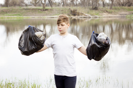 young volunteer guy picks up trash on the banks of the spring river. Global problem. Spring cleaning areaの写真素材
