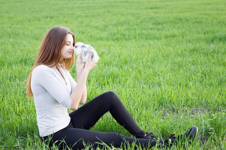 Girl holding a rabbit while on a green meadow. Young smiling girl holding a little fluffy white rabbit. Friendship with Easter Bunny. Spring photo with beautiful young girl with her Bunnyの写真素材