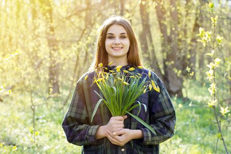 Girl in the forest with a bouquet of yellow flowers. The girl is holding forest yellow tulips. Girl in spring forestの写真素材
