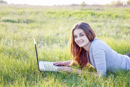 girl working in nature with a laptop lying on the green grass. The girl works as a freelance traveler. Freelancer with a laptop in natureの写真素材
