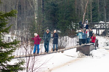 Saint Petersburg. RUSSIA . January 2, 2020. a group of tourists walk on a pedestrian bridge in nature in the winter . Hiking in coniferous forests. Group nature walkの写真素材