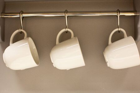 three mugs weigh on hangers in a home corner in the kitchen. Household utensils in quick access. Convenient location of the circle in the kitchenの写真素材